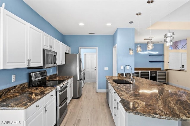 kitchen featuring sink, hanging light fixtures, stainless steel appliances, dark stone counters, and white cabinets