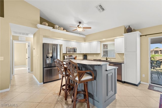 kitchen featuring white cabinets, light tile patterned flooring, a kitchen island, and stainless steel appliances