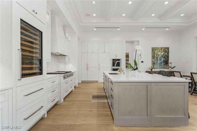 kitchen with beamed ceiling, a spacious island, white cabinetry, and premium range hood