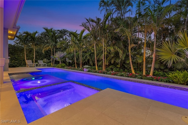 pool at dusk with an in ground hot tub and a patio