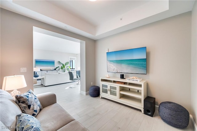 living room with light wood-type flooring and a tray ceiling