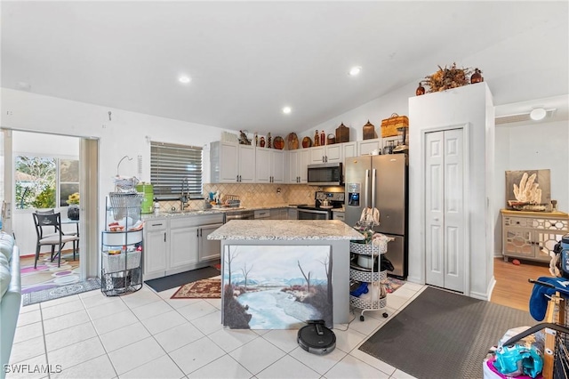 kitchen featuring a center island, sink, stainless steel appliances, backsplash, and lofted ceiling