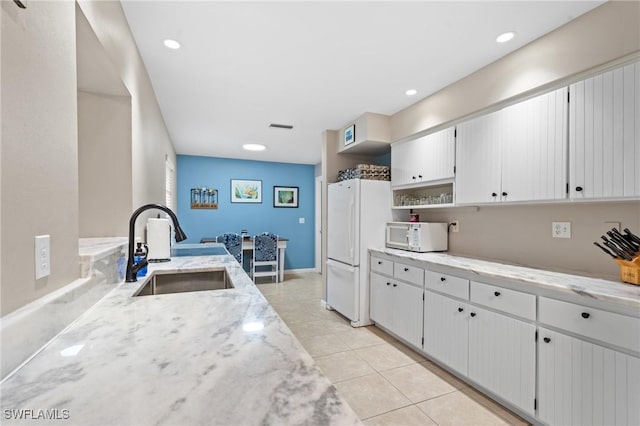 kitchen featuring white appliances, white cabinets, sink, light stone countertops, and light tile patterned floors