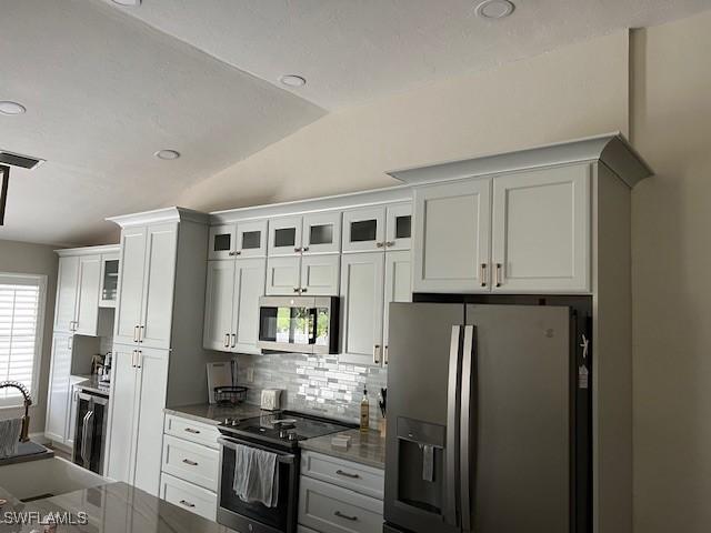 kitchen with appliances with stainless steel finishes, tasteful backsplash, sink, white cabinets, and lofted ceiling