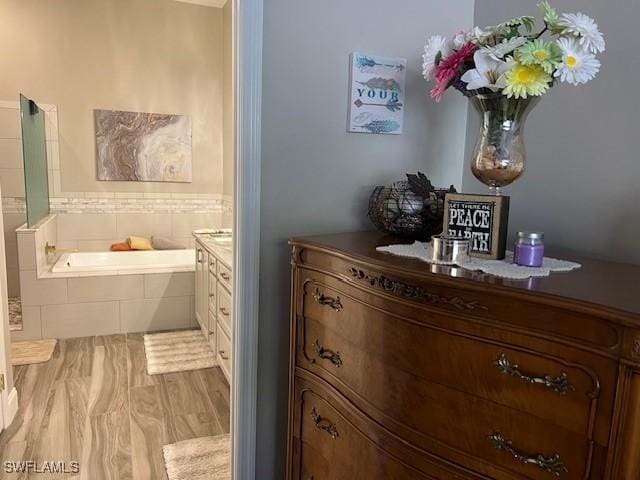 bathroom featuring hardwood / wood-style flooring, vanity, and a relaxing tiled tub