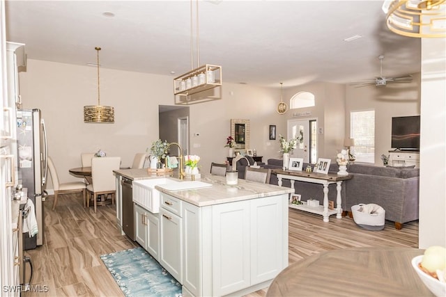 kitchen with pendant lighting, appliances with stainless steel finishes, white cabinetry, a kitchen island with sink, and light stone counters