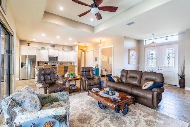 living room with a tray ceiling, french doors, and ceiling fan