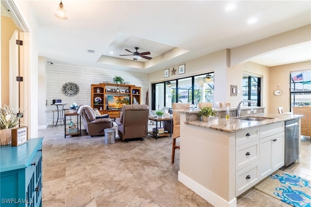 kitchen featuring sink, white cabinetry, light stone counters, a tray ceiling, and a kitchen island with sink