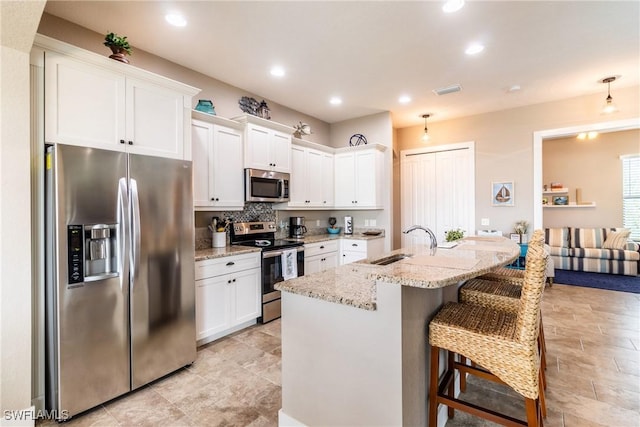 kitchen featuring white cabinetry, a center island with sink, light stone countertops, and appliances with stainless steel finishes