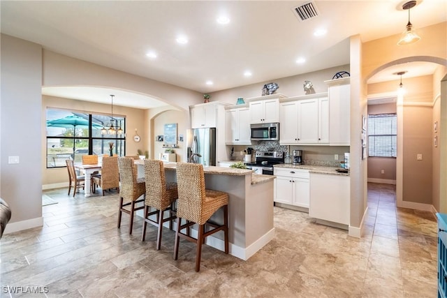 kitchen with pendant lighting, stainless steel appliances, light stone countertops, and a center island with sink