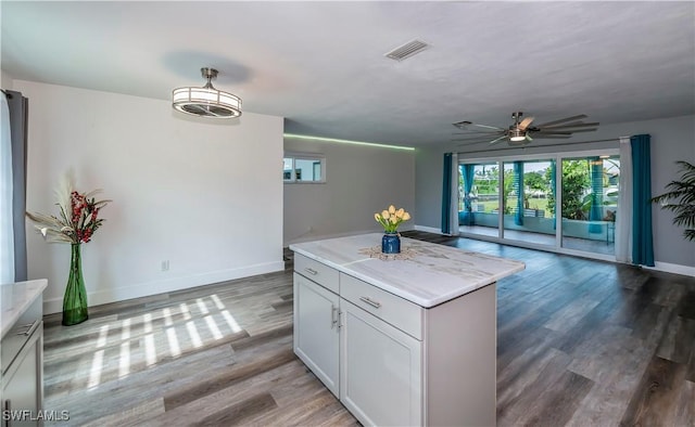 kitchen featuring ceiling fan, a kitchen island, wood-type flooring, and white cabinetry