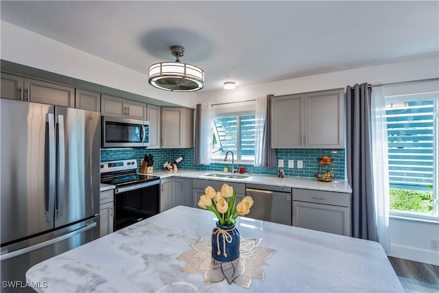 kitchen with tasteful backsplash, light stone counters, stainless steel appliances, sink, and gray cabinets