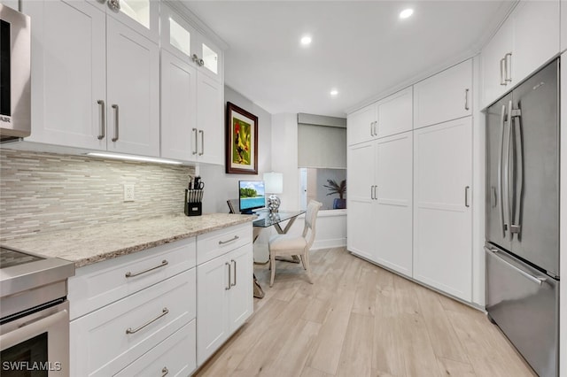 kitchen with white cabinets, light stone counters, stainless steel fridge, and light wood-type flooring