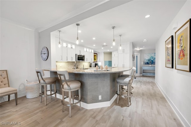 kitchen with a breakfast bar, tasteful backsplash, white cabinetry, kitchen peninsula, and light wood-type flooring