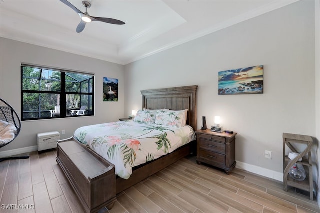 bedroom featuring ceiling fan, a raised ceiling, light wood-type flooring, and ornamental molding