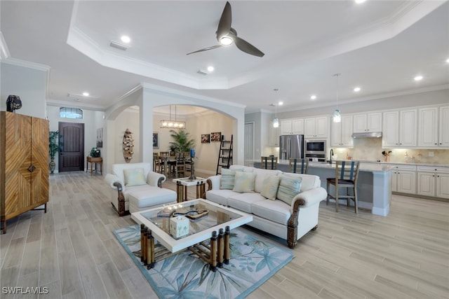 living room with a tray ceiling, crown molding, and ceiling fan with notable chandelier