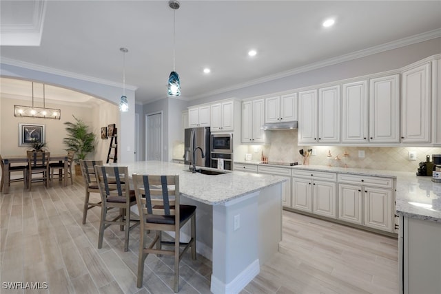 kitchen featuring backsplash, decorative light fixtures, a center island with sink, white cabinets, and a breakfast bar area