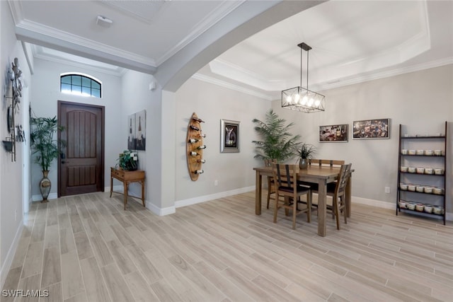 dining space featuring a raised ceiling, light hardwood / wood-style flooring, ornamental molding, and a notable chandelier