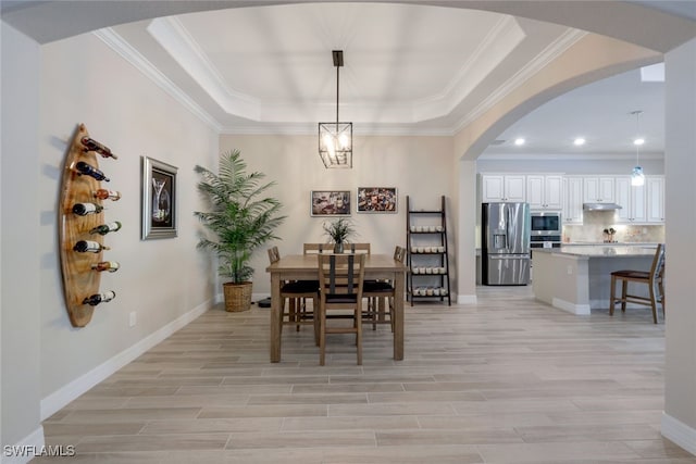 dining space with a raised ceiling, light wood-style flooring, baseboards, and arched walkways