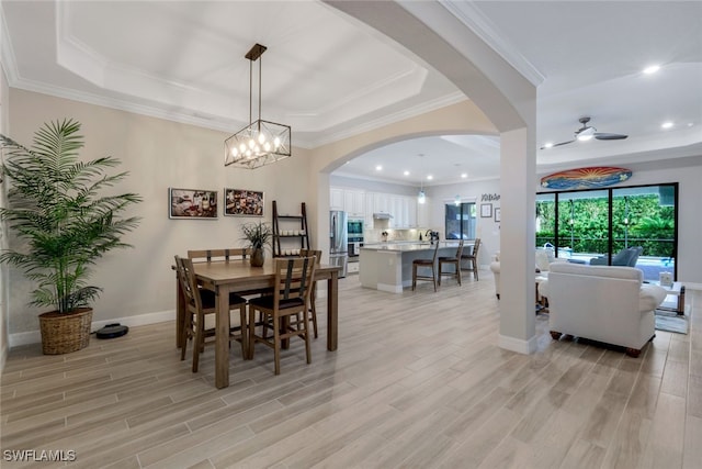 dining space featuring ceiling fan with notable chandelier, light hardwood / wood-style floors, a raised ceiling, and ornamental molding