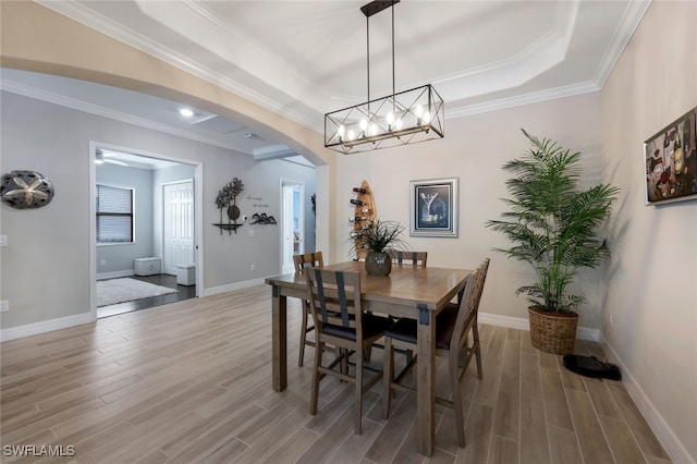 dining area with ornamental molding, a tray ceiling, wood finished floors, arched walkways, and baseboards