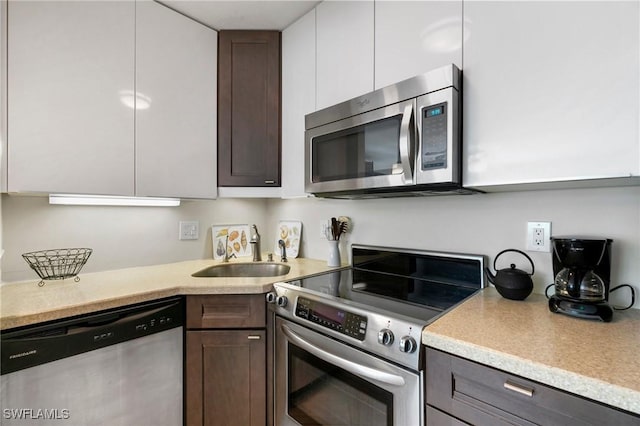 kitchen with dark brown cabinetry, white cabinetry, sink, and appliances with stainless steel finishes