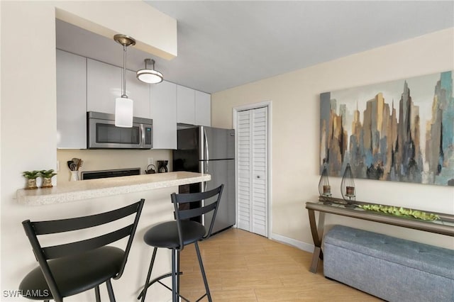 kitchen with a kitchen breakfast bar, white cabinetry, hanging light fixtures, and stainless steel appliances