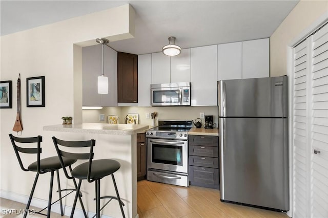 kitchen with dark brown cabinetry, stainless steel appliances, a kitchen breakfast bar, decorative light fixtures, and white cabinets