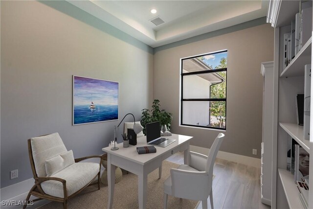 home office featuring a tray ceiling and light hardwood / wood-style flooring