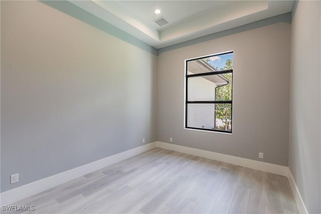 spare room with a raised ceiling and light hardwood / wood-style flooring