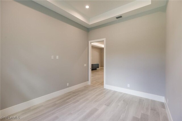 spare room with a tray ceiling and light hardwood / wood-style floors