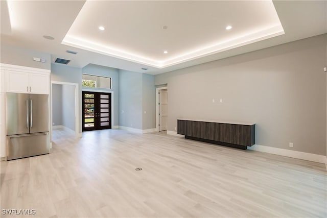 unfurnished living room with a tray ceiling, light hardwood / wood-style flooring, and french doors