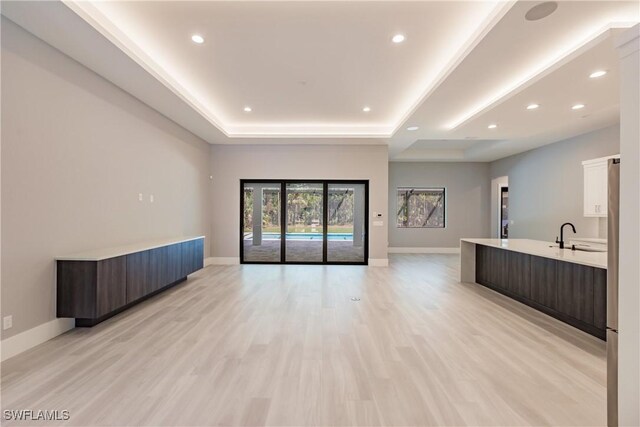 unfurnished living room featuring a raised ceiling, light wood-type flooring, and sink