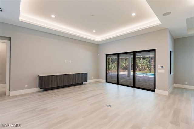 spare room with light hardwood / wood-style floors and a raised ceiling