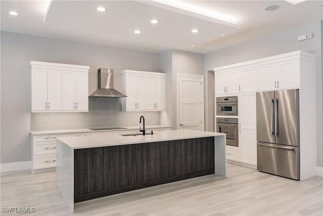 kitchen with sink, stainless steel appliances, a kitchen island with sink, and wall chimney range hood