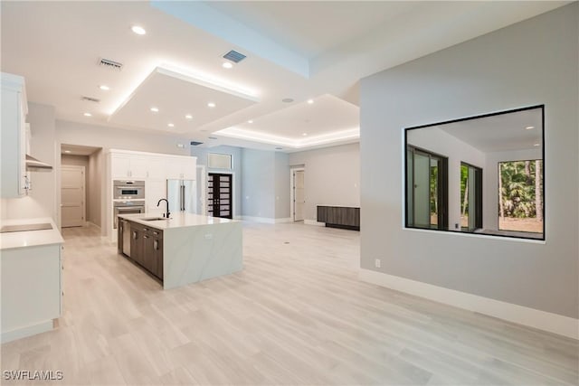 kitchen featuring a kitchen island with sink, a raised ceiling, sink, white cabinetry, and stainless steel appliances