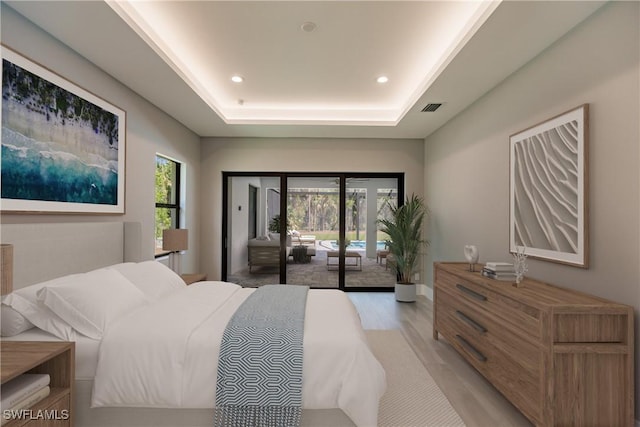 bedroom with a raised ceiling, access to outside, and light hardwood / wood-style flooring