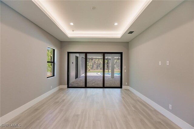 spare room featuring light hardwood / wood-style floors and a raised ceiling