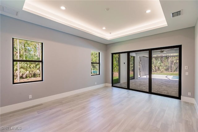 empty room with a tray ceiling, ceiling fan, a healthy amount of sunlight, and light wood-type flooring