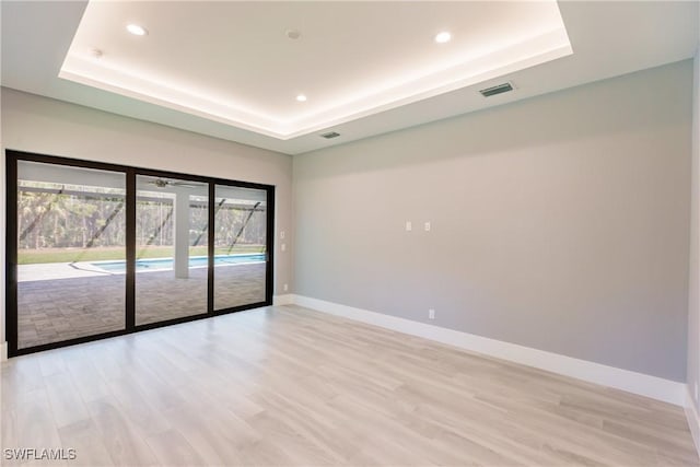 spare room featuring light hardwood / wood-style floors and a raised ceiling