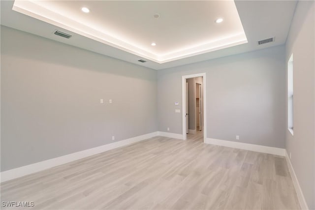 empty room featuring a tray ceiling and light hardwood / wood-style floors