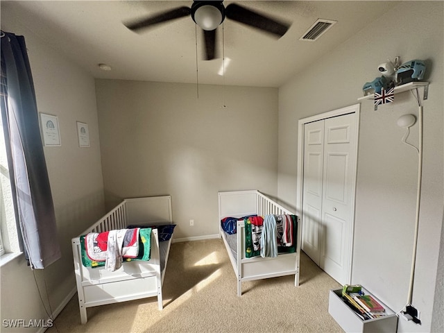 bedroom with ceiling fan, a crib, and light carpet