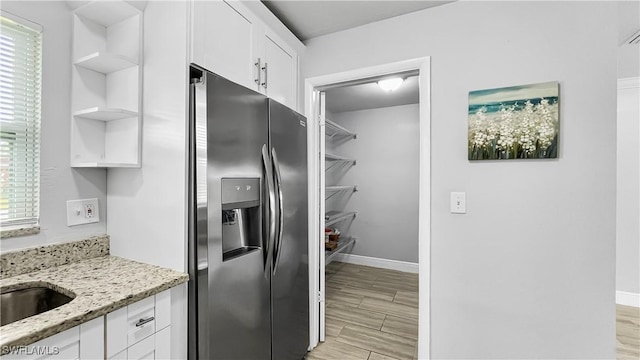 kitchen featuring white cabinets, stainless steel refrigerator with ice dispenser, light stone counters, and a healthy amount of sunlight