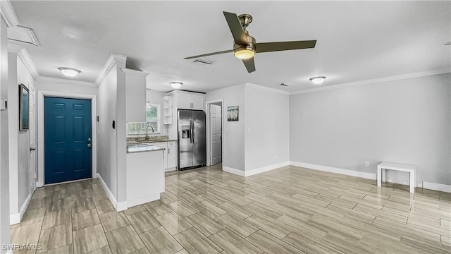 kitchen featuring ceiling fan, sink, stainless steel fridge, crown molding, and white cabinets