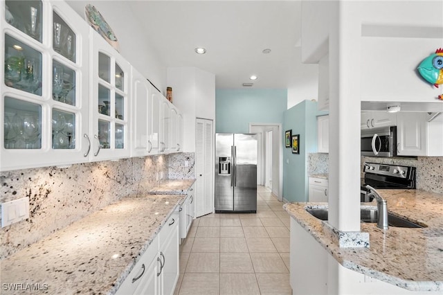 kitchen featuring light tile patterned flooring, light stone counters, white cabinets, stainless steel appliances, and backsplash