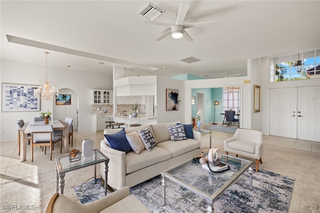 living room with light tile patterned floors, ceiling fan with notable chandelier, visible vents, and light carpet