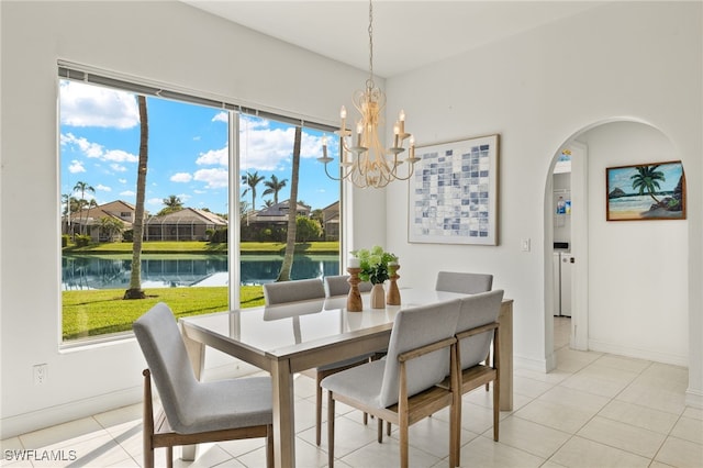 dining room with arched walkways, a notable chandelier, light tile patterned floors, and a water view