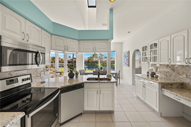 kitchen featuring light stone counters, a peninsula, a sink, appliances with stainless steel finishes, and tasteful backsplash