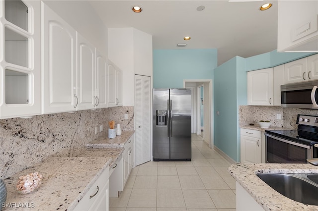 kitchen with white cabinets, light tile patterned floors, light stone countertops, and appliances with stainless steel finishes