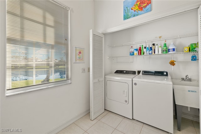 laundry area featuring baseboards, light tile patterned floors, laundry area, independent washer and dryer, and a sink